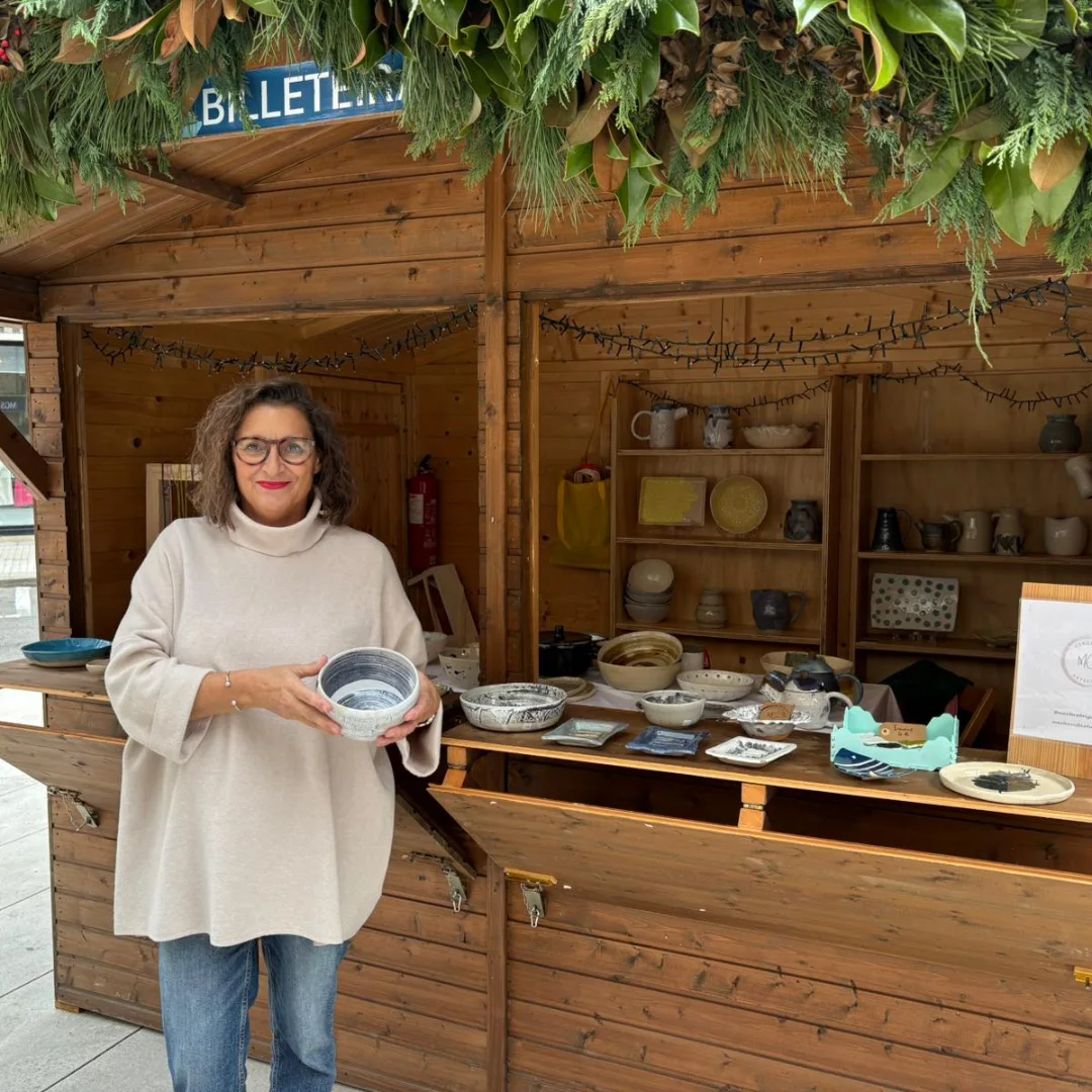 Marta sosteniendo un cuenco frente al puesto del mercado navideño